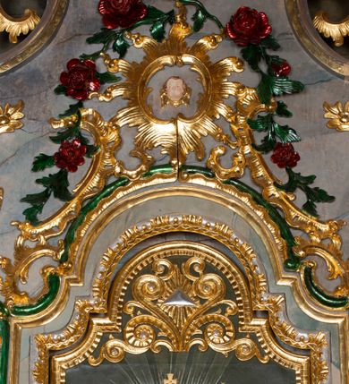 Zdjęcie nr 12: Nastawa ołtarzowa drewniana, architektoniczna, jednoosiowa, jednokondygnacyjna ze zwieńczeniem. Mensa w typie sarkofagowym, wklęsło-wypukła, zwężająca się ku dołowi, zamknięta gzymsem; naroża ujęte fragmentami rocaille&#039;u, na froncie rocaille’owy kartusz; portatyl z marmuru dębnickiego. Na mensie ustawiono tabernakulum w formie prostopadłościennej skrzynki, o wypukłej ściance frontowej, która jest ujęta w narożach ustawionymi pod kątem pilastrami na cokołach, których trzony przyjmują formę spływów wolutowych. Podpory dźwigają gzyms, opasujący całą skrzynkę, wyłamany na ich osi. Drzwiczki w formie stojącego prostokąta zamkniętego łukiem nadwieszonym, w polu nisza z płaskorzeźbionym przedstawieniem kielicha z hostią w glorii. Drzwiczki zostały ujęte płyciną w formie stojącego prostokąta zamkniętego łukiem kotarowym dwudzielnym. Na tabernakulum tron wystawienia w postaci cokołu. Nastawa ołtarzowa została posadowiona na wysokim cokole, przyjmującym po bokach formę wolut stanowiących podstawę dla figur św. Piotra z prawej i św. Pawła z lewej strony. Jest ujęta parą pilastrów ustawionych pod katem względem lica, których trzony u góry przechodzą w woluty. Podpory dźwigają imposty. W polu środkowym płycina w formie stojącego prostokąta zamkniętego łukiem półkolistym nadwieszonym z uskokiem, w której znajduje się mniejsza nisza o tej samej formie, ujęta ramą, wypełniona obrazem Matki Boskiej z Dzieciątkiem. Zwieńczenie w formie zbliżonej do trapezu, ujętego podwójnymi spływami wolutowymi, zamkniętego falistym gzymsem. Całość wieńczy rzeźbiona gołębica Ducha Świętego w glorii promienistej. Trzony pilastrów nastawy dekorowane zwisami z różanych gałązek. Płycina pola środkowego ujęta rocaille&#039;em, który ponad łukiem, w polu zwieńczenia, tworzy medalion z uskrzydloną główką anielską, otoczony dużymi różanymi gałązkami; w polu środkowym cztery uskrzydlone główki anielskie. Kondygnacja flankowana uszami utworzonymi z płomienistego rocaille&#039;u i różanych gałązek. Na belkowaniu dwa rokokowe wazony z różami. Zwieńczenie ujęte falbanką, rocaille&#039;em i różanymi gałązkami. Struktura w całości marmoryzowana w kolorze szaroniebieskim, ornamentyki i profile złocone i srebrzone, ukwiecone gałązki laserunkowe.