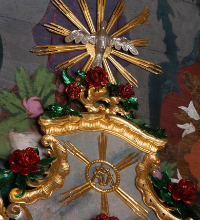 Zdjęcie nr 15: Nastawa ołtarzowa drewniana, architektoniczna, jednoosiowa, jednokondygnacyjna ze zwieńczeniem. Mensa w typie sarkofagowym, wklęsło-wypukła, zwężająca się ku dołowi, zamknięta gzymsem; naroża ujęte fragmentami rocaille'u, na froncie rocaille’owy kartusz; portatyl z marmuru dębnickiego. Na mensie ustawiono tabernakulum w formie prostopadłościennej skrzynki, o wypukłej ściance frontowej, która jest ujęta w narożach ustawionymi pod kątem pilastrami na cokołach, których trzony przyjmują formę spływów wolutowych. Podpory dźwigają gzyms, opasujący całą skrzynkę, wyłamany na ich osi. Drzwiczki w formie stojącego prostokąta zamkniętego łukiem nadwieszonym, w polu nisza z płaskorzeźbionym przedstawieniem kielicha z hostią w glorii. Drzwiczki zostały ujęte płyciną w formie stojącego prostokąta zamkniętego łukiem kotarowym dwudzielnym. Na tabernakulum tron wystawienia w postaci cokołu. Nastawa ołtarzowa została posadowiona na wysokim cokole, przyjmującym po bokach formę wolut stanowiących podstawę dla figur św. Piotra z prawej i św. Pawła z lewej strony. Jest ujęta parą pilastrów ustawionych pod katem względem lica, których trzony u góry przechodzą w woluty. Podpory dźwigają imposty. W polu środkowym płycina w formie stojącego prostokąta zamkniętego łukiem półkolistym nadwieszonym z uskokiem, w której znajduje się mniejsza nisza o tej samej formie, ujęta ramą, wypełniona obrazem Matki Boskiej z Dzieciątkiem. Zwieńczenie w formie zbliżonej do trapezu, ujętego podwójnymi spływami wolutowymi, zamkniętego falistym gzymsem. Całość wieńczy rzeźbiona gołębica Ducha Świętego w glorii promienistej. Trzony pilastrów nastawy dekorowane zwisami z różanych gałązek. Płycina pola środkowego ujęta rocaille'em, który ponad łukiem, w polu zwieńczenia, tworzy medalion z uskrzydloną główką anielską, otoczony dużymi różanymi gałązkami; w polu środkowym cztery uskrzydlone główki anielskie. Kondygnacja flankowana uszami utworzonymi z płomienistego rocaille'u i różanych gałązek. Na belkowaniu dwa rokokowe wazony z różami. Zwieńczenie ujęte falbanką, rocaille'em i różanymi gałązkami. Struktura w całości marmoryzowana w kolorze szaroniebieskim, ornamentyki i profile złocone i srebrzone, ukwiecone gałązki laserunkowe.