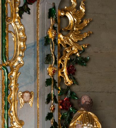 Zdjęcie nr 6: Nastawa ołtarzowa drewniana, architektoniczna, jednoosiowa, jednokondygnacyjna ze zwieńczeniem. Mensa w typie sarkofagowym, wklęsło-wypukła, zwężająca się ku dołowi, zamknięta gzymsem; naroża ujęte fragmentami rocaille'u, na froncie rocaille’owy kartusz; portatyl z marmuru dębnickiego. Na mensie ustawiono tabernakulum w formie prostopadłościennej skrzynki, o wypukłej ściance frontowej, która jest ujęta w narożach ustawionymi pod kątem pilastrami na cokołach, których trzony przyjmują formę spływów wolutowych. Podpory dźwigają gzyms, opasujący całą skrzynkę, wyłamany na ich osi. Drzwiczki w formie stojącego prostokąta zamkniętego łukiem nadwieszonym, w polu nisza z płaskorzeźbionym przedstawieniem kielicha z hostią w glorii. Drzwiczki zostały ujęte płyciną w formie stojącego prostokąta zamkniętego łukiem kotarowym dwudzielnym. Na tabernakulum tron wystawienia w postaci cokołu. Nastawa ołtarzowa została posadowiona na wysokim cokole, przyjmującym po bokach formę wolut stanowiących podstawę dla figur św. Piotra z prawej i św. Pawła z lewej strony. Jest ujęta parą pilastrów ustawionych pod katem względem lica, których trzony u góry przechodzą w woluty. Podpory dźwigają imposty. W polu środkowym płycina w formie stojącego prostokąta zamkniętego łukiem półkolistym nadwieszonym z uskokiem, w której znajduje się mniejsza nisza o tej samej formie, ujęta ramą, wypełniona obrazem Matki Boskiej z Dzieciątkiem. Zwieńczenie w formie zbliżonej do trapezu, ujętego podwójnymi spływami wolutowymi, zamkniętego falistym gzymsem. Całość wieńczy rzeźbiona gołębica Ducha Świętego w glorii promienistej. Trzony pilastrów nastawy dekorowane zwisami z różanych gałązek. Płycina pola środkowego ujęta rocaille'em, który ponad łukiem, w polu zwieńczenia, tworzy medalion z uskrzydloną główką anielską, otoczony dużymi różanymi gałązkami; w polu środkowym cztery uskrzydlone główki anielskie. Kondygnacja flankowana uszami utworzonymi z płomienistego rocaille'u i różanych gałązek. Na belkowaniu dwa rokokowe wazony z różami. Zwieńczenie ujęte falbanką, rocaille'em i różanymi gałązkami. Struktura w całości marmoryzowana w kolorze szaroniebieskim, ornamentyki i profile złocone i srebrzone, ukwiecone gałązki laserunkowe.