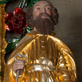 Zdjęcie nr 1: Rzeźba ścięta z tyłu została ustawiona na podstawie w formie kostki o ściętych narożach. Figura jest zwrócona frontalnie, w delikatnym kontrapoście. Święty ma obie ręce, ugięte, uniesione, w dłoniach trzyma klucze – w prawej srebrny, w lewej złoty. Twarz ma pociągłą, szczupłą, o płytko osadzonych oczach, krótkim, prostym nosie i okoloną falowaną, opadającą na pierś brodą. Włosy wywinięte w loki, gęste, sięgają karku. Święty Piotr jest ubrany w złotą tunikę z długimi, wąskimi rękawami, przepasaną w talii srebrną wstęgą, zawiązaną z przodu na węzeł, drapowaną w liczne, równoległe fałdki oraz złoty płaszcz zapięty pod szyją, opadający na ramiona i delikatnie drapowany. Polichromia naturalistyczna w odsłoniętych partiach ciała. 