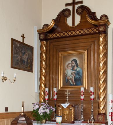 Zdjęcie nr 1: Nastawa ołtarzowa przyścienna, architektoniczna, jednokondygnacyjna ze zwieńczeniem. Mensa skrzyniowa, prostopadłościenna, ustawiona na jednym stopniu. Antepedium trójpolowe, obramione profilowanymi listwami, w narożach ujęte skręconymi, złoconymi kolumnami. W środkowym polu hierogram IHS, w bocznych motywy kwiatu dziewięćsiłu. Portatyl w formie kamiennej płytki. Tabernakulum w kształcie niewielkiej prostopadłościennej szafki, ujęte w narożach skręconymi kolumnami o kapitelach kostkowych, podtrzymujących profilowany gzyms. Od frontu drzwiczki w formie prostokąta zamkniętego łukiem odcinkowym, z rytą dekoracją roślinną i aplikowanym złoconym kielichem. Nastawa płaska, flankowana skręconymi, złoconymi kolumnami, ustawionymi na cokołach, dekorowanych rozetką. Kolumny zwieńczone kostkowymi kapitelami z rozetkami, nad którymi przerwany przyczółek. Nad polem środkowym zredukowane belkowanie, z fryzem zdobionym ukośną kratką. Zwieńczenie ujęte dwoma wolutami z uskokiem, dekorowanymi na krańcach rozetkami pomiędzy którymi półokrągłe wycięcie i łaciński krzyż. W polu głównym obraz św. Józefa z Dzieciątkiem w prostokątnej ramie, dookoła obwiedziony szerokim profilowaniem. Struktura bejcowana, pokryta lakierem, detale i kolumny złocone. 
