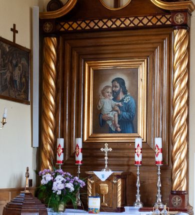 Zdjęcie nr 3: Nastawa ołtarzowa przyścienna, architektoniczna, jednokondygnacyjna ze zwieńczeniem. Mensa skrzyniowa, prostopadłościenna, ustawiona na jednym stopniu. Antepedium trójpolowe, obramione profilowanymi listwami, w narożach ujęte skręconymi, złoconymi kolumnami. W środkowym polu hierogram IHS, w bocznych motywy kwiatu dziewięćsiłu. Portatyl w formie kamiennej płytki. Tabernakulum w kształcie niewielkiej prostopadłościennej szafki, ujęte w narożach skręconymi kolumnami o kapitelach kostkowych, podtrzymujących profilowany gzyms. Od frontu drzwiczki w formie prostokąta zamkniętego łukiem odcinkowym, z rytą dekoracją roślinną i aplikowanym złoconym kielichem. Nastawa płaska, flankowana skręconymi, złoconymi kolumnami, ustawionymi na cokołach, dekorowanych rozetką. Kolumny zwieńczone kostkowymi kapitelami z rozetkami, nad którymi przerwany przyczółek. Nad polem środkowym zredukowane belkowanie, z fryzem zdobionym ukośną kratką. Zwieńczenie ujęte dwoma wolutami z uskokiem, dekorowanymi na krańcach rozetkami pomiędzy którymi półokrągłe wycięcie i łaciński krzyż. W polu głównym obraz św. Józefa z Dzieciątkiem w prostokątnej ramie, dookoła obwiedziony szerokim profilowaniem. Struktura bejcowana, pokryta lakierem, detale i kolumny złocone. 
