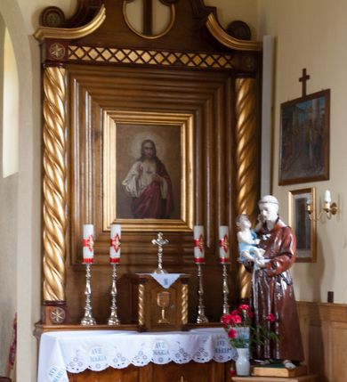 Zdjęcie nr 2: Nastawa ołtarzowa przyścienna, architektoniczna, jednokondygnacyjna ze zwieńczeniem. Mensa skrzyniowa, prostopadłościenna, ustawiona na jednym stopniu. Antepedium trójpolowe, obramione profilowanymi listwami, w narożach ujęte skręconymi, złoconymi kolumnami. W środkowym polu hierogram IHS, w bocznych motywy kwiatu dziewięćsiłu. Portatyl w formie kamiennej płytki. Tabernakulum w kształcie niewielkiej prostopadłościennej szafki, ujęte w narożach skręconymi kolumnami o kapitelach kostkowych, podtrzymujących profilowany gzyms. Od frontu drzwiczki w formie prostokąta zamkniętego łukiem odcinkowym, z rytą dekoracją roślinną i aplikowanym złoconym kielichem. Nastawa płaska, flankowana skręconymi, złoconymi kolumnami, ustawionymi na cokołach, dekorowanych rozetką. Kolumny zwieńczone kostkowymi kapitelami, ozdobionymi rozetką, nad którymi przerwany przyczółek. Nad polem środkowym zredukowane belkowanie, z fryzem zdobionym ukośną kratką. Zwieńczenie ujęte dwoma wolutami z uskokiem, dekorowanymi na krańcach rozetkami, pomiędzy którymi półokrągłe wycięcie i łaciński krzyż. W polu głównym obraz „Najświętsze Serce Jezusa” w prostokątnej ramie, dookoła obwiedziony szerokim profilowaniem. Struktura bejcowana, pokryta lakierem, detale i kolumny złocone. 