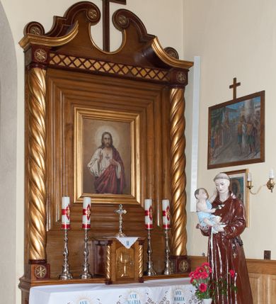 Zdjęcie nr 1: Nastawa ołtarzowa przyścienna, architektoniczna, jednokondygnacyjna ze zwieńczeniem. Mensa skrzyniowa, prostopadłościenna, ustawiona na jednym stopniu. Antepedium trójpolowe, obramione profilowanymi listwami, w narożach ujęte skręconymi, złoconymi kolumnami. W środkowym polu hierogram IHS, w bocznych motywy kwiatu dziewięćsiłu. Portatyl w formie kamiennej płytki. Tabernakulum w kształcie niewielkiej prostopadłościennej szafki, ujęte w narożach skręconymi kolumnami o kapitelach kostkowych, podtrzymujących profilowany gzyms. Od frontu drzwiczki w formie prostokąta zamkniętego łukiem odcinkowym, z rytą dekoracją roślinną i aplikowanym złoconym kielichem. Nastawa płaska, flankowana skręconymi, złoconymi kolumnami, ustawionymi na cokołach, dekorowanych rozetką. Kolumny zwieńczone kostkowymi kapitelami, ozdobionymi rozetką, nad którymi przerwany przyczółek. Nad polem środkowym zredukowane belkowanie, z fryzem zdobionym ukośną kratką. Zwieńczenie ujęte dwoma wolutami z uskokiem, dekorowanymi na krańcach rozetkami, pomiędzy którymi półokrągłe wycięcie i łaciński krzyż. W polu głównym obraz „Najświętsze Serce Jezusa” w prostokątnej ramie, dookoła obwiedziony szerokim profilowaniem. Struktura bejcowana, pokryta lakierem, detale i kolumny złocone. 