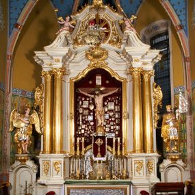 Zdjęcie nr 1: Ołtarz prostopadłościenny z mensą. Antepedium w formie leżącego prostokąta ujętego drewnianą, profilowaną ramą z przedstawieniem Mandylionu i narzędziami Męki Pańskiej na tle wypełnionym ornamentem roślinnym. W centrum, u dołu dwie tarcze herbowe z inicjałami: „TR” i „W”.
Nastawa ołtarzowa architektoniczna, jednoosiowa z bramkami, jednokondygnacyjna ze zwieńczeniem, ustawiona na dwustrefowym cokole. Ujęta dwiema parami kolumn o kapitelach korynckich, ustawionych uskokowo na cokołach zdobionych ornamentem rocaille, dźwigających pełne belkowanie wyłamane na ich osi, nad polem głównym przerwany architraw i fryz oraz gzyms przyjmujący kształt łuku odcinkowego. Na belkowaniu wewnętrznej pary kolumn przerwany wolutowy przyczółek z siedzącymi na nim puttami z narzędziami Męki Pańskiej. W polu głównym wnęka o wykroju prostokąta stojącego zamkniętego łukiem odcinkowym nadwieszonym, w złotej ramie dekorowanej rocaille, w której znajduje się krucyfiks na tle czerwonego atłasu obwieszonego wotami. Powyżej, w partii belkowania rocaillowy kartusz z napisem: „HOC OPUS / NOSTRAE / SALUTIS”. Ołtarz ujęty ażurowymi uszami utworzonymi z ornamentu rocaille.  Zwieńczenie ujęte spływami wolutowymi, zamknięte dwiema skierowanymi do środka wolutami, dekorowane ornamentem rocaille. W polu płycina w formie stojącego owalu wyłożona czerwonym atłasem, ujęta profilowaną ramą z rzeźbą gołębicy Ducha Świętego na tle obłoków w glorii promienistej, flankowana przez akant przechodzący w woluty oraz przez kwiatowe festony z wstęgą. Bramki o wykroju stojącego prostokąta, zamkniętego łukiem odcinkowym nadwieszonym z drzwiczkami, zakończone konsolami ujętymi spływami wolutowymi, stanowiącymi podstawy dla figur św. Michała Archanioła i św. Wacława. Struktura ołtarza malowana na kolor biały, z pozłacaną ornamentyką profilami i kolumnami.

