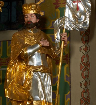 Zdjęcie nr 20: Ołtarz prostopadłościenny z mensą. Antepedium w formie leżącego prostokąta ujętego drewnianą, profilowaną ramą z przedstawieniem Mandylionu i narzędziami Męki Pańskiej na tle wypełnionym ornamentem roślinnym. W centrum, u dołu dwie tarcze herbowe z inicjałami: „TR” i „W”.
Nastawa ołtarzowa architektoniczna, jednoosiowa z bramkami, jednokondygnacyjna ze zwieńczeniem, ustawiona na dwustrefowym cokole. Ujęta dwiema parami kolumn o kapitelach korynckich, ustawionych uskokowo na cokołach zdobionych ornamentem rocaille, dźwigających pełne belkowanie wyłamane na ich osi, nad polem głównym przerwany architraw i fryz oraz gzyms przyjmujący kształt łuku odcinkowego. Na belkowaniu wewnętrznej pary kolumn przerwany wolutowy przyczółek z siedzącymi na nim puttami z narzędziami Męki Pańskiej. W polu głównym wnęka o wykroju prostokąta stojącego zamkniętego łukiem odcinkowym nadwieszonym, w złotej ramie dekorowanej rocaille, w której znajduje się krucyfiks na tle czerwonego atłasu obwieszonego wotami. Powyżej, w partii belkowania rocaillowy kartusz z napisem: „HOC OPUS / NOSTRAE / SALUTIS”. Ołtarz ujęty ażurowymi uszami utworzonymi z ornamentu rocaille.  Zwieńczenie ujęte spływami wolutowymi, zamknięte dwiema skierowanymi do środka wolutami, dekorowane ornamentem rocaille. W polu płycina w formie stojącego owalu wyłożona czerwonym atłasem, ujęta profilowaną ramą z rzeźbą gołębicy Ducha Świętego na tle obłoków w glorii promienistej, flankowana przez akant przechodzący w woluty oraz przez kwiatowe festony z wstęgą. Bramki o wykroju stojącego prostokąta, zamkniętego łukiem odcinkowym nadwieszonym z drzwiczkami, zakończone konsolami ujętymi spływami wolutowymi, stanowiącymi podstawy dla figur św. Michała Archanioła i św. Wacława. Struktura ołtarza malowana na kolor biały, z pozłacaną ornamentyką profilami i kolumnami.

