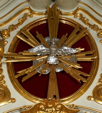 Zdjęcie nr 27: Ołtarz prostopadłościenny z mensą. Antepedium w formie leżącego prostokąta ujętego drewnianą, profilowaną ramą z przedstawieniem Mandylionu i narzędziami Męki Pańskiej na tle wypełnionym ornamentem roślinnym. W centrum, u dołu dwie tarcze herbowe z inicjałami: „TR” i „W”.
Nastawa ołtarzowa architektoniczna, jednoosiowa z bramkami, jednokondygnacyjna ze zwieńczeniem, ustawiona na dwustrefowym cokole. Ujęta dwiema parami kolumn o kapitelach korynckich, ustawionych uskokowo na cokołach zdobionych ornamentem rocaille, dźwigających pełne belkowanie wyłamane na ich osi, nad polem głównym przerwany architraw i fryz oraz gzyms przyjmujący kształt łuku odcinkowego. Na belkowaniu wewnętrznej pary kolumn przerwany wolutowy przyczółek z siedzącymi na nim puttami z narzędziami Męki Pańskiej. W polu głównym wnęka o wykroju prostokąta stojącego zamkniętego łukiem odcinkowym nadwieszonym, w złotej ramie dekorowanej rocaille, w której znajduje się krucyfiks na tle czerwonego atłasu obwieszonego wotami. Powyżej, w partii belkowania rocaillowy kartusz z napisem: „HOC OPUS / NOSTRAE / SALUTIS”. Ołtarz ujęty ażurowymi uszami utworzonymi z ornamentu rocaille.  Zwieńczenie ujęte spływami wolutowymi, zamknięte dwiema skierowanymi do środka wolutami, dekorowane ornamentem rocaille. W polu płycina w formie stojącego owalu wyłożona czerwonym atłasem, ujęta profilowaną ramą z rzeźbą gołębicy Ducha Świętego na tle obłoków w glorii promienistej, flankowana przez akant przechodzący w woluty oraz przez kwiatowe festony z wstęgą. Bramki o wykroju stojącego prostokąta, zamkniętego łukiem odcinkowym nadwieszonym z drzwiczkami, zakończone konsolami ujętymi spływami wolutowymi, stanowiącymi podstawy dla figur św. Michała Archanioła i św. Wacława. Struktura ołtarza malowana na kolor biały, z pozłacaną ornamentyką profilami i kolumnami.

