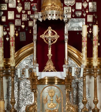 Zdjęcie nr 24: Ołtarz prostopadłościenny z mensą. Antepedium w formie leżącego prostokąta ujętego drewnianą, profilowaną ramą z przedstawieniem Mandylionu i narzędziami Męki Pańskiej na tle wypełnionym ornamentem roślinnym. W centrum, u dołu dwie tarcze herbowe z inicjałami: „TR” i „W”.
Nastawa ołtarzowa architektoniczna, jednoosiowa z bramkami, jednokondygnacyjna ze zwieńczeniem, ustawiona na dwustrefowym cokole. Ujęta dwiema parami kolumn o kapitelach korynckich, ustawionych uskokowo na cokołach zdobionych ornamentem rocaille, dźwigających pełne belkowanie wyłamane na ich osi, nad polem głównym przerwany architraw i fryz oraz gzyms przyjmujący kształt łuku odcinkowego. Na belkowaniu wewnętrznej pary kolumn przerwany wolutowy przyczółek z siedzącymi na nim puttami z narzędziami Męki Pańskiej. W polu głównym wnęka o wykroju prostokąta stojącego zamkniętego łukiem odcinkowym nadwieszonym, w złotej ramie dekorowanej rocaille, w której znajduje się krucyfiks na tle czerwonego atłasu obwieszonego wotami. Powyżej, w partii belkowania rocaillowy kartusz z napisem: „HOC OPUS / NOSTRAE / SALUTIS”. Ołtarz ujęty ażurowymi uszami utworzonymi z ornamentu rocaille.  Zwieńczenie ujęte spływami wolutowymi, zamknięte dwiema skierowanymi do środka wolutami, dekorowane ornamentem rocaille. W polu płycina w formie stojącego owalu wyłożona czerwonym atłasem, ujęta profilowaną ramą z rzeźbą gołębicy Ducha Świętego na tle obłoków w glorii promienistej, flankowana przez akant przechodzący w woluty oraz przez kwiatowe festony z wstęgą. Bramki o wykroju stojącego prostokąta, zamkniętego łukiem odcinkowym nadwieszonym z drzwiczkami, zakończone konsolami ujętymi spływami wolutowymi, stanowiącymi podstawy dla figur św. Michała Archanioła i św. Wacława. Struktura ołtarza malowana na kolor biały, z pozłacaną ornamentyką profilami i kolumnami.

