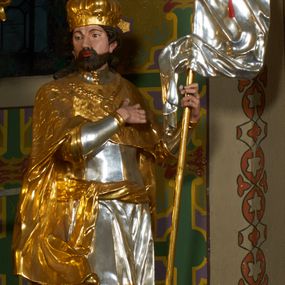 Zdjęcie nr 1: Rzeźba drążona z tyłu, ustawiona na podstawie o nieregularnym planie. Święty ukazany w całej postaci, frontalnie, z głową skierowaną w prawą stronę, stojący w kontrapoście. Prawa ręka postaci spoczywa na piersi, lewą trzyma drzewce zwiniętej chorągwi zakończone krzyżem, na srebrnym płacie chorągwi widoczny czerwony krzyż. Wacław ma szeroką twarz o migdałowatych oczach, dużym nosie i pełnych ustach, okoloną krótką brodą oraz silnie kręconymi włosami opadającymi na ramiona. Ubrany jest w zbroję oraz tunikę widoczną w partii ud, przepasaną w biodrach wstęgą. Ramiona i plecy przykrywa płaszcz z imitującą futro gronostajowe pelerynką, na piersi ma zawieszony łańcuch z krzyżem, na głowie zaś mitrę książęcą. Polichromia figury jest naturalistyczna w partiach ciała, zbroja i tunika srebrzone, płaszcz, mitra i detale stroju złocone. 