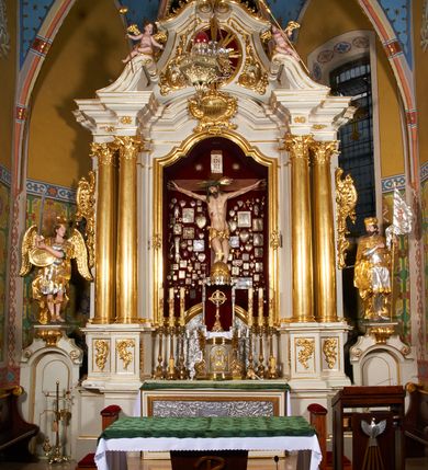 Zdjęcie nr 6: Krzyż drewniany o prostych ramionach z figurą w typie Cristo vivo przybitą trzema gwoździami. Sylwetka w lekkim zwisie, o szerokim rozłożeniu ramion, z głową przechyloną na prawe ramię; nogi ugięte w kolanach, skierowane w prawą stronę, stopy w układzie prawa na lewą. Twarz pociągła o wąskich, otwartych oczach, dużym nosie, otwartych ustach, okolona brodą oraz włosami skręconymi w rurkowate pukle. Na głowie korona cierniowa, wokół niej trzy wiązki promieni. Ciało wychudzone, o zaznaczonych mięśniach ramion i nóg oraz sumarycznie kształtowanej klatce piersiowej z podkreślonymi liniami żeber i wypukłością brzucha oraz ze śladami męki w postaci rzeźbionych kropel krwi wypływającej z ran. Perizonium krótkie, ściśle opinające biodra, zawiązane w partii podbrzusza, ze zwisem na prawym biodrze. Na górnym zakończeniu pionowej belki krzyża banderola z napisem „INRI”. Ciało polichromowane naturalistycznie, perizonium pozłacane. 
