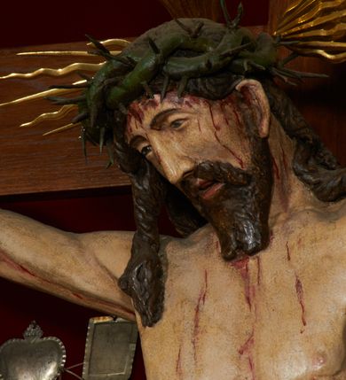 Zdjęcie nr 9: Krzyż drewniany o prostych ramionach z figurą w typie Cristo vivo przybitą trzema gwoździami. Sylwetka w lekkim zwisie, o szerokim rozłożeniu ramion, z głową przechyloną na prawe ramię; nogi ugięte w kolanach, skierowane w prawą stronę, stopy w układzie prawa na lewą. Twarz pociągła o wąskich, otwartych oczach, dużym nosie, otwartych ustach, okolona brodą oraz włosami skręconymi w rurkowate pukle. Na głowie korona cierniowa, wokół niej trzy wiązki promieni. Ciało wychudzone, o zaznaczonych mięśniach ramion i nóg oraz sumarycznie kształtowanej klatce piersiowej z podkreślonymi liniami żeber i wypukłością brzucha oraz ze śladami męki w postaci rzeźbionych kropel krwi wypływającej z ran. Perizonium krótkie, ściśle opinające biodra, zawiązane w partii podbrzusza, ze zwisem na prawym biodrze. Na górnym zakończeniu pionowej belki krzyża banderola z napisem „INRI”. Ciało polichromowane naturalistycznie, perizonium pozłacane. 
