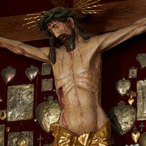 Zdjęcie nr 1: Krzyż drewniany o prostych ramionach z figurą w typie Cristo vivo przybitą trzema gwoździami. Sylwetka w lekkim zwisie, o szerokim rozłożeniu ramion, z głową przechyloną na prawe ramię; nogi ugięte w kolanach, skierowane w prawą stronę, stopy w układzie prawa na lewą. Twarz pociągła o wąskich, otwartych oczach, dużym nosie, otwartych ustach, okolona brodą oraz włosami skręconymi w rurkowate pukle. Na głowie korona cierniowa, wokół niej trzy wiązki promieni. Ciało wychudzone, o zaznaczonych mięśniach ramion i nóg oraz sumarycznie kształtowanej klatce piersiowej z podkreślonymi liniami żeber i wypukłością brzucha oraz ze śladami męki w postaci rzeźbionych kropel krwi wypływającej z ran. Perizonium krótkie, ściśle opinające biodra, zawiązane w partii podbrzusza, ze zwisem na prawym biodrze. Na górnym zakończeniu pionowej belki krzyża banderola z napisem „INRI”. Ciało polichromowane naturalistycznie, perizonium pozłacane. 

