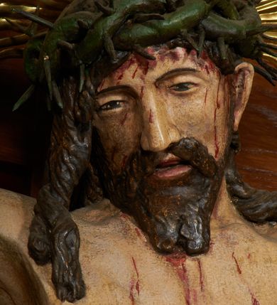 Zdjęcie nr 11: Krzyż drewniany o prostych ramionach z figurą w typie Cristo vivo przybitą trzema gwoździami. Sylwetka w lekkim zwisie, o szerokim rozłożeniu ramion, z głową przechyloną na prawe ramię; nogi ugięte w kolanach, skierowane w prawą stronę, stopy w układzie prawa na lewą. Twarz pociągła o wąskich, otwartych oczach, dużym nosie, otwartych ustach, okolona brodą oraz włosami skręconymi w rurkowate pukle. Na głowie korona cierniowa, wokół niej trzy wiązki promieni. Ciało wychudzone, o zaznaczonych mięśniach ramion i nóg oraz sumarycznie kształtowanej klatce piersiowej z podkreślonymi liniami żeber i wypukłością brzucha oraz ze śladami męki w postaci rzeźbionych kropel krwi wypływającej z ran. Perizonium krótkie, ściśle opinające biodra, zawiązane w partii podbrzusza, ze zwisem na prawym biodrze. Na górnym zakończeniu pionowej belki krzyża banderola z napisem „INRI”. Ciało polichromowane naturalistycznie, perizonium pozłacane. 
