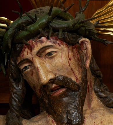 Zdjęcie nr 12: Krzyż drewniany o prostych ramionach z figurą w typie Cristo vivo przybitą trzema gwoździami. Sylwetka w lekkim zwisie, o szerokim rozłożeniu ramion, z głową przechyloną na prawe ramię; nogi ugięte w kolanach, skierowane w prawą stronę, stopy w układzie prawa na lewą. Twarz pociągła o wąskich, otwartych oczach, dużym nosie, otwartych ustach, okolona brodą oraz włosami skręconymi w rurkowate pukle. Na głowie korona cierniowa, wokół niej trzy wiązki promieni. Ciało wychudzone, o zaznaczonych mięśniach ramion i nóg oraz sumarycznie kształtowanej klatce piersiowej z podkreślonymi liniami żeber i wypukłością brzucha oraz ze śladami męki w postaci rzeźbionych kropel krwi wypływającej z ran. Perizonium krótkie, ściśle opinające biodra, zawiązane w partii podbrzusza, ze zwisem na prawym biodrze. Na górnym zakończeniu pionowej belki krzyża banderola z napisem „INRI”. Ciało polichromowane naturalistycznie, perizonium pozłacane. 
