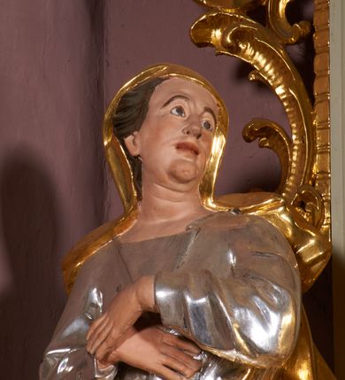Zdjęcie nr 4: Nastawa ołtarzowa architektoniczna, jednoosiowa, jednokondygnacyjna ze zwieńczeniem, ustawiona na dwustrefowym cokole, z wyodrębnionymi po bokach dwoma prostopadłościennymi postumentami. Ołtarz drewniany, prostopadłościenny. Antepedium w formie poziomego prostokąta w profilowanej ramie, jego powierzchnia podzielona jest wstęgami na trzy owalne pola, wewnątrz każdego wazon z bukietem kwiatów z owocami, dookoła nich w niewielkich polach przedstawienia orłów. Na mensie ustawione tabernakulum w formie prostopadłościennej skrzynki z drzwiczkami w formie pionowego prostokąta, z przedstawieniem hostii w glorii promienistej.
Środkowa część struktury nastawy ujęta parą kolumn kompozytowych na tle zwielokrotnionych pilastrów, ustawionych na wyodrębnionych cokołach dekorowanych rocaille'm. Kolumny dźwigają pełne belkowanie wyłamane na ich osi oraz odcinki przerwanego, falistego przyczółka, na którym siedzą putta. W polu środkowym obraz z przedstawieniem Matki Boskiej Niepokalanie Poczętej ze św. Heleną i św. Wojciechem w formie pionowego prostokąta zamkniętego łukiem półkolistym, w profilowanej ramie dekorowanej rocaille'm. Nad obrazem, w partii belkowania rocaille'owy kartusz z napisem „TOTA / PULCHRA EST MARIA / ET MACULA ORDINATIS/ IN TE”. Po zewnętrznej stronie kolumn na wspornikach stoją figury św. Anny i św. Joachima. Ołtarz flankowany uszami utworzonymi z motywów rocaille. Zwieńczenie w formie trapezu ujętego spływami wolutowymi, zamkniętego łukiem półkolistym nadwieszonym, obwiedzionego profilowanymi listwami, zwieńczonego gzymsem, dekorowanym rocaiile'owym kartuszem i ornamentem roślinnym. W polu powtarzającym kształt zwieńczenia obraz Narodzenia Marii w profilowanej ramie. Struktura ołtarza polichromowana w kolorze bieli, ornamentyka, profile i kolumny pozłacane.





