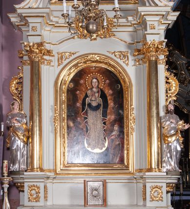 Zdjęcie nr 1: Nastawa ołtarzowa architektoniczna, jednoosiowa, jednokondygnacyjna ze zwieńczeniem, ustawiona na dwustrefowym cokole, z wyodrębnionymi po bokach dwoma prostopadłościennymi postumentami. Ołtarz drewniany, prostopadłościenny. Antepedium w formie poziomego prostokąta w profilowanej ramie, jego powierzchnia podzielona jest wstęgami na trzy owalne pola, wewnątrz każdego wazon z bukietem kwiatów z owocami, dookoła nich w niewielkich polach przedstawienia orłów. Na mensie ustawione tabernakulum w formie prostopadłościennej skrzynki z drzwiczkami w formie pionowego prostokąta, z przedstawieniem hostii w glorii promienistej.
Środkowa część struktury nastawy ujęta parą kolumn kompozytowych na tle zwielokrotnionych pilastrów, ustawionych na wyodrębnionych cokołach dekorowanych rocaille'm. Kolumny dźwigają pełne belkowanie wyłamane na ich osi oraz odcinki przerwanego, falistego przyczółka, na którym siedzą putta. W polu środkowym obraz z przedstawieniem Matki Boskiej Niepokalanie Poczętej ze św. Heleną i św. Wojciechem w formie pionowego prostokąta zamkniętego łukiem półkolistym, w profilowanej ramie dekorowanej rocaille'm. Nad obrazem, w partii belkowania rocaille'owy kartusz z napisem „TOTA / PULCHRA EST MARIA / ET MACULA ORDINATIS/ IN TE”. Po zewnętrznej stronie kolumn na wspornikach stoją figury św. Anny i św. Joachima. Ołtarz flankowany uszami utworzonymi z motywów rocaille. Zwieńczenie w formie trapezu ujętego spływami wolutowymi, zamkniętego łukiem półkolistym nadwieszonym, obwiedzionego profilowanymi listwami, zwieńczonego gzymsem, dekorowanym rocaiile'owym kartuszem i ornamentem roślinnym. W polu powtarzającym kształt zwieńczenia obraz Narodzenia Marii w profilowanej ramie. Struktura ołtarza polichromowana w kolorze bieli, ornamentyka, profile i kolumny pozłacane.





