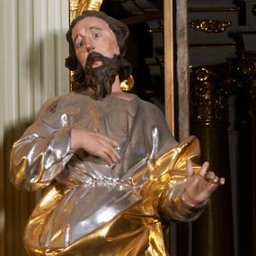 Zdjęcie nr 1: Rzeźba z tyłu drążona, ustawiona na niewielkiej, prostej podstawie. Joachim przedstawiony w całej postaci, ustawiony  frontalnie, z głową skierowaną w prawo, stojąc w kontrapoście, odchylony jest delikatnie w tył. Prawa dłoń świętego spoczywa na piersi, lewa wyciągnięta jest do przodu, w geście przemowy. Twarz świętego jest szczupła i pociągła, o dużych oczach z głęboko rzeźbionymi powiekami oraz uniesionymi brwiami. Nos ma prosty, usta pełne, rozchylone, okolona jest gęstą, kręconą brodą oraz włosami sięgającymi ramion, układającymi się w głęboko rzeźbione pukle. Święty ubrany jest w długą tunikę przepasaną w talii, obficie drapowaną i przylegającą do ciała oraz w płaszcz opasujący diagonalnie postać, zawieszony na lewym przedramieniu świętego z rozwianym zwisem tkaniny na lewym boku. Figura polichromowana naturalistycznie w partiach ciała, broda i włosy brązowe, tunika srebrzona, płaszcz złocony.
