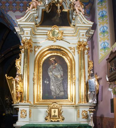 Zdjęcie nr 1: Nastawa ołtarzowa architektoniczna, jednoosiowa, jednokondygnacyjna ze zwieńczeniem, ustawiona na dwustrefowym cokole, z wyodrębnionymi po bokach dwoma prostopadłościennymi postumentami. Ołtarz drewniany, prostopadłościenny. Antepedium w formie poziomego prostokąta w profilowanej ramie, w polu podzielone jest wstęgami na trzy owalne pola, wewnątrz każdego korona w wieńcu z ornamentu roślinnego, dookoła w niewielkich polach ptaki z gałązkami w dziobach. Na mensie ustawione tabernakulum w formie prostopadłościennej skrzynki, ujętej spływami wolutowymi, zwieńczonej motywem rocaille. Drzwiczki w formie pionowego prostokąta, w profilowanej ramie z rytym przedstawieniem kielicha z hostią na obłoku. 
Środkowa część struktury nastawy ujęta parą kolumn kompozytowych ustawionych na tle zwielokrotnionych pilastrów oraz na wyodrębnionych cokołach dekorowanych rocaille&#039;m. Kolumny dźwigają pełne belkowanie wyłamane na ich osi oraz odcinki przerwanego, falistego przyczółka z siedzącymi na nich puttami. W polu środkowym obraz z przedstawieniem św. Józefa w formie pionowego prostokąta zamkniętego łukiem półkolistym, w profilowanej ramie dekorowanej rocaille&#039;m. Nad obrazem, w partii belkowania rocaille&#039;owy kartusz z napisem „SANCTE / JOSEPH / INTERCEDE / PRO NOBIS”. Po zewnętrznej stronie kolumn na wspornikach stoją figury Dawida i Mojżesza. Ołtarz flankowany uszami utworzonymi z motywów rocaille. Zwieńczenie w formie trapezu ujętego spływami wolutowymi, zamkniętego łukiem półkolistym nadwieszonym, obwiedzionego profilowanymi listwami, zwieńczonego gzymsem, dekorowanym kartuszem z motywów rocaille. W polu powtarzającym kształt zwieńczenia obraz św. Kryspina z Viterbo w profilowanej ramie. Struktura ołtarza polichromowana w kolorze bieli, ornamentyka, profile i kolumny pozłacane.

