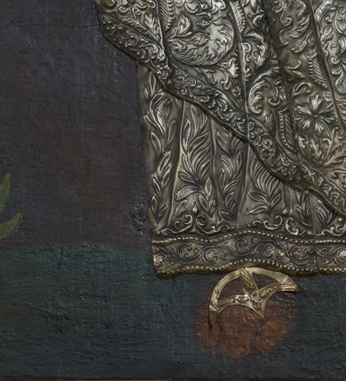 Zdjęcie nr 4: Obraz w kształcie stojącego prostokąta, zamkniętego łukiem półkolistym. W centrum kompozycji ukazany św. Józef w postawie stojącej, delikatnie zwrócony w prawą stronę, z prawą stopą wysuniętą do przodu a prawą ręką złożoną na piersi, zaś lewą ręką przytrzymujący połę płaszcza u boku. Twarz świętego owalna, z długim i prostym nosem, okolona siwą brodą oraz długimi i delikatnie siwymi włosami, opadającymi na ramiona. Postać przykryta metalową sukienką w kolorze srebra, na powierzchni której oddano przebieg draperii szat świętego oraz zdobiący je ornament roślinny, a nad głową złoconą, kameryzowaną i promienistą koronę. Tło jednolite, brunatne, wokół głowy św. Józefa delikatnie rozjaśnione na kształt nimbu. Po lewej stronie obrazu krzak białej lilii. 


