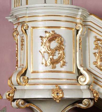 Zdjęcie nr 1: Ambona wisząca, przyścienna, z dostępem od strony północnej w formie podestu z balustradą, prowadzącego do drzwi przekutych w murze. Kosz na planie zbliżonym do kwadratu, o wklęsło-wypukłych ściankach, na cokole dekorowanym rocaille'em, z podwieszeniem w formie stożka ujętego spływami wolutowymi i zakończonego szyszką. Ścianki kosza ujęte w narożach pilastrami o trzonach w formie spływów wolutowych dekorowanych kampanulami, podtrzymujących belkowanie z gzymsem tworzącym parapet. Na ściankach płyciny zdobione rocaille'em. Balustrada podestu pełna, dekorowana płycinami ze stylizowanym ornamentem roślinnym. Zaplecek flankowany pilastrami o kanelowanych trzonach, o kapitelach w formie konsol dźwigających imposty oraz fragmenty przerwanego, wolutowego, odwróconego na zewnątrz przyczółka. W polu zaplecka płycina w kształcie stojącego prostokąta o wklęsłych narożach, z malowanym krzyżem ujętym wieńcem laurowym i tablicami Dekalogu. Zaplecek flankowany uszami w formie stylizowanego rocaille'u. Całość zwieńczona rzeźbą gołębicy Ducha Świętego w glorii promienistej. Struktura ambony polichromowana na kolor biały, profile i ornamentyka złocone, detale srebrzone. 