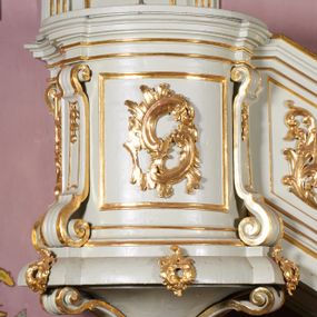 Zdjęcie nr 1: Ambona wisząca, przyścienna, z dostępem od strony północnej w formie podestu z balustradą, prowadzącego do drzwi przekutych w murze. Kosz na planie zbliżonym do kwadratu, o wklęsło-wypukłych ściankach, na cokole dekorowanym rocaille'em, z podwieszeniem w formie stożka ujętego spływami wolutowymi i zakończonego szyszką. Ścianki kosza ujęte w narożach pilastrami o trzonach w formie spływów wolutowych dekorowanych kampanulami, podtrzymujących belkowanie z gzymsem tworzącym parapet. Na ściankach płyciny zdobione rocaille'em. Balustrada podestu pełna, dekorowana płycinami ze stylizowanym ornamentem roślinnym. Zaplecek flankowany pilastrami o kanelowanych trzonach, o kapitelach w formie konsol dźwigających imposty oraz fragmenty przerwanego, wolutowego, odwróconego na zewnątrz przyczółka. W polu zaplecka płycina w kształcie stojącego prostokąta o wklęsłych narożach, z malowanym krzyżem ujętym wieńcem laurowym i tablicami Dekalogu. Zaplecek flankowany uszami w formie stylizowanego rocaille'u. Całość zwieńczona rzeźbą gołębicy Ducha Świętego w glorii promienistej. Struktura ambony polichromowana na kolor biały, profile i ornamentyka złocone, detale srebrzone. 