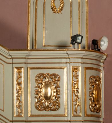 Zdjęcie nr 3: Ambona wisząca, przyścienna, z dostępem od strony północnej w formie podestu z balustradą, prowadzącego do drzwi przekutych w murze. Kosz na planie zbliżonym do kwadratu, o wklęsło-wypukłych ściankach, na cokole dekorowanym rocaille&#039;em, z podwieszeniem w formie stożka ujętego spływami wolutowymi i zakończonego szyszką. Ścianki kosza ujęte w narożach pilastrami o trzonach w formie spływów wolutowych dekorowanych kampanulami, podtrzymujących belkowanie z gzymsem tworzącym parapet. Na ściankach płyciny zdobione rocaille&#039;em. Balustrada podestu pełna, dekorowana płycinami ze stylizowanym ornamentem roślinnym. Zaplecek flankowany pilastrami o kanelowanych trzonach, o kapitelach w formie konsol dźwigających imposty oraz fragmenty przerwanego, wolutowego, odwróconego na zewnątrz przyczółka. W polu zaplecka płycina w kształcie stojącego prostokąta o wklęsłych narożach, z malowanym krzyżem ujętym wieńcem laurowym i tablicami Dekalogu. Zaplecek flankowany uszami w formie stylizowanego rocaille&#039;u. Całość zwieńczona rzeźbą gołębicy Ducha Świętego w glorii promienistej. Struktura ambony polichromowana na kolor biały, profile i ornamentyka złocone, detale srebrzone. 