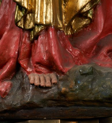 Zdjęcie nr 9: Rzeźba pełnoplastyczna, przyścienna, drążona od tyłu, ustawiona na konsoli. Maria stoi w lekkim kontrapoście, ciężar ciała opierając na lewej nodze, prawą lekko uginając w kolanie. Lewą ręką podtrzymuje siedzące na jej ramieniu Dzieciątko, w prawej ugiętej w łokciu i wysuniętej lekko do przodu trzyma błyskawicę. Twarz pociągła, z długim, prostym, wąskim nosem, oczami o migdałowym wykroju, regularnymi łukami brwiowymi oraz wąskimi ustami, okolona długimi, ciemnobrązowymi włosami, z przedziałkiem pośrodku głowy, opadającymi na ramiona dwoma skręcającymi się w pukle pasmami. Maria ubrana w długą, czerwoną suknię z wąskimi rękawami oraz złoty płaszcz spięty na piersi, przerzucony z przodu przez lewe ramię, układający się pośrodku w trzy płytkie misowe fałdy, po bokach formujący się w dwa festony. Dzieciątko siedzi wyprostowane w ramionach Matki, zwrócone przodem do widza, w prawej rączce trzymając krzyż, w lewej jabłko królewskie. Głowa pochylona lekko na lewe ramię; okrągła twarz z małym, zadartym nosem, wąskimi ustami, niewielkimi oczami i regularnymi łukami brwiowymi, okolona krótkimi ciemnobrązowymi włosami. Jezus ubrany w długą białą szatę układającą się w proste, bardzo płytkie fałdy. Na głowach nowsze korony otwarte.