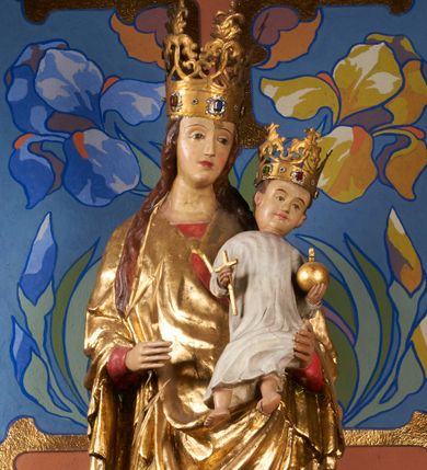 Zdjęcie nr 1: Rzeźba pełnoplastyczna, przyścienna, drążona od tyłu, ustawiona na konsoli. Maria stoi w lekkim kontrapoście, ciężar ciała opierając na lewej nodze, prawą lekko uginając w kolanie. Lewą ręką podtrzymuje siedzące na jej ramieniu Dzieciątko, w prawej ugiętej w łokciu i wysuniętej lekko do przodu trzyma błyskawicę. Twarz pociągła, z długim, prostym, wąskim nosem, oczami o migdałowym wykroju, regularnymi łukami brwiowymi oraz wąskimi ustami, okolona długimi, ciemnobrązowymi włosami, z przedziałkiem pośrodku głowy, opadającymi na ramiona dwoma skręcającymi się w pukle pasmami. Maria ubrana w długą, czerwoną suknię z wąskimi rękawami oraz złoty płaszcz spięty na piersi, przerzucony z przodu przez lewe ramię, układający się pośrodku w trzy płytkie misowe fałdy, po bokach formujący się w dwa festony. Dzieciątko siedzi wyprostowane w ramionach Matki, zwrócone przodem do widza, w prawej rączce trzymając krzyż, w lewej jabłko królewskie. Głowa pochylona lekko na lewe ramię; okrągła twarz z małym, zadartym nosem, wąskimi ustami, niewielkimi oczami i regularnymi łukami brwiowymi, okolona krótkimi ciemnobrązowymi włosami. Jezus ubrany w długą białą szatę układającą się w proste, bardzo płytkie fałdy. Na głowach nowsze korony otwarte.