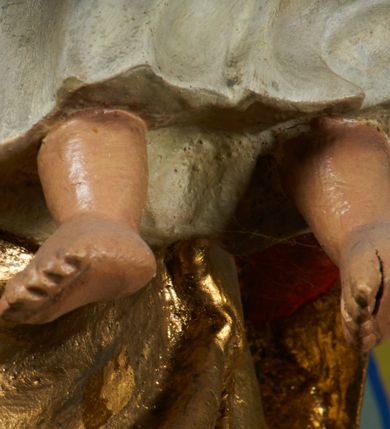 Zdjęcie nr 4: Rzeźba pełnoplastyczna, przyścienna, drążona od tyłu, ustawiona na konsoli. Maria stoi w lekkim kontrapoście, ciężar ciała opierając na lewej nodze, prawą lekko uginając w kolanie. Lewą ręką podtrzymuje siedzące na jej ramieniu Dzieciątko, w prawej ugiętej w łokciu i wysuniętej lekko do przodu trzyma błyskawicę. Twarz pociągła, z długim, prostym, wąskim nosem, oczami o migdałowym wykroju, regularnymi łukami brwiowymi oraz wąskimi ustami, okolona długimi, ciemnobrązowymi włosami, z przedziałkiem pośrodku głowy, opadającymi na ramiona dwoma skręcającymi się w pukle pasmami. Maria ubrana w długą, czerwoną suknię z wąskimi rękawami oraz złoty płaszcz spięty na piersi, przerzucony z przodu przez lewe ramię, układający się pośrodku w trzy płytkie misowe fałdy, po bokach formujący się w dwa festony. Dzieciątko siedzi wyprostowane w ramionach Matki, zwrócone przodem do widza, w prawej rączce trzymając krzyż, w lewej jabłko królewskie. Głowa pochylona lekko na lewe ramię; okrągła twarz z małym, zadartym nosem, wąskimi ustami, niewielkimi oczami i regularnymi łukami brwiowymi, okolona krótkimi ciemnobrązowymi włosami. Jezus ubrany w długą białą szatę układającą się w proste, bardzo płytkie fałdy. Na głowach nowsze korony otwarte.