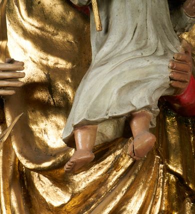 Zdjęcie nr 6: Rzeźba pełnoplastyczna, przyścienna, drążona od tyłu, ustawiona na konsoli. Maria stoi w lekkim kontrapoście, ciężar ciała opierając na lewej nodze, prawą lekko uginając w kolanie. Lewą ręką podtrzymuje siedzące na jej ramieniu Dzieciątko, w prawej ugiętej w łokciu i wysuniętej lekko do przodu trzyma błyskawicę. Twarz pociągła, z długim, prostym, wąskim nosem, oczami o migdałowym wykroju, regularnymi łukami brwiowymi oraz wąskimi ustami, okolona długimi, ciemnobrązowymi włosami, z przedziałkiem pośrodku głowy, opadającymi na ramiona dwoma skręcającymi się w pukle pasmami. Maria ubrana w długą, czerwoną suknię z wąskimi rękawami oraz złoty płaszcz spięty na piersi, przerzucony z przodu przez lewe ramię, układający się pośrodku w trzy płytkie misowe fałdy, po bokach formujący się w dwa festony. Dzieciątko siedzi wyprostowane w ramionach Matki, zwrócone przodem do widza, w prawej rączce trzymając krzyż, w lewej jabłko królewskie. Głowa pochylona lekko na lewe ramię; okrągła twarz z małym, zadartym nosem, wąskimi ustami, niewielkimi oczami i regularnymi łukami brwiowymi, okolona krótkimi ciemnobrązowymi włosami. Jezus ubrany w długą białą szatę układającą się w proste, bardzo płytkie fałdy. Na głowach nowsze korony otwarte.