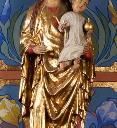 Zdjęcie nr 2: Rzeźba pełnoplastyczna, przyścienna, drążona od tyłu, ustawiona na konsoli. Maria stoi w lekkim kontrapoście, ciężar ciała opierając na lewej nodze, prawą lekko uginając w kolanie. Lewą ręką podtrzymuje siedzące na jej ramieniu Dzieciątko, w prawej ugiętej w łokciu i wysuniętej lekko do przodu trzyma błyskawicę. Twarz pociągła, z długim, prostym, wąskim nosem, oczami o migdałowym wykroju, regularnymi łukami brwiowymi oraz wąskimi ustami, okolona długimi, ciemnobrązowymi włosami, z przedziałkiem pośrodku głowy, opadającymi na ramiona dwoma skręcającymi się w pukle pasmami. Maria ubrana w długą, czerwoną suknię z wąskimi rękawami oraz złoty płaszcz spięty na piersi, przerzucony z przodu przez lewe ramię, układający się pośrodku w trzy płytkie misowe fałdy, po bokach formujący się w dwa festony. Dzieciątko siedzi wyprostowane w ramionach Matki, zwrócone przodem do widza, w prawej rączce trzymając krzyż, w lewej jabłko królewskie. Głowa pochylona lekko na lewe ramię; okrągła twarz z małym, zadartym nosem, wąskimi ustami, niewielkimi oczami i regularnymi łukami brwiowymi, okolona krótkimi ciemnobrązowymi włosami. Jezus ubrany w długą białą szatę układającą się w proste, bardzo płytkie fałdy. Na głowach nowsze korony otwarte.