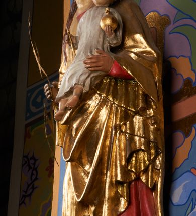 Zdjęcie nr 5: Rzeźba pełnoplastyczna, przyścienna, drążona od tyłu, ustawiona na konsoli. Maria stoi w lekkim kontrapoście, ciężar ciała opierając na lewej nodze, prawą lekko uginając w kolanie. Lewą ręką podtrzymuje siedzące na jej ramieniu Dzieciątko, w prawej ugiętej w łokciu i wysuniętej lekko do przodu trzyma błyskawicę. Twarz pociągła, z długim, prostym, wąskim nosem, oczami o migdałowym wykroju, regularnymi łukami brwiowymi oraz wąskimi ustami, okolona długimi, ciemnobrązowymi włosami, z przedziałkiem pośrodku głowy, opadającymi na ramiona dwoma skręcającymi się w pukle pasmami. Maria ubrana w długą, czerwoną suknię z wąskimi rękawami oraz złoty płaszcz spięty na piersi, przerzucony z przodu przez lewe ramię, układający się pośrodku w trzy płytkie misowe fałdy, po bokach formujący się w dwa festony. Dzieciątko siedzi wyprostowane w ramionach Matki, zwrócone przodem do widza, w prawej rączce trzymając krzyż, w lewej jabłko królewskie. Głowa pochylona lekko na lewe ramię; okrągła twarz z małym, zadartym nosem, wąskimi ustami, niewielkimi oczami i regularnymi łukami brwiowymi, okolona krótkimi ciemnobrązowymi włosami. Jezus ubrany w długą białą szatę układającą się w proste, bardzo płytkie fałdy. Na głowach nowsze korony otwarte.