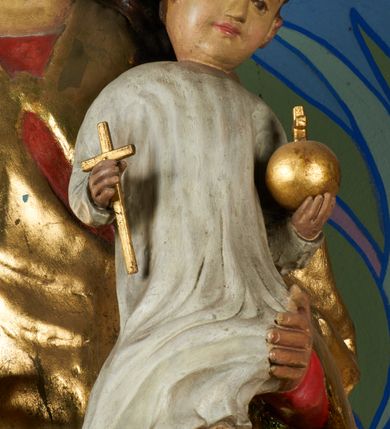 Zdjęcie nr 8: Rzeźba pełnoplastyczna, przyścienna, drążona od tyłu, ustawiona na konsoli. Maria stoi w lekkim kontrapoście, ciężar ciała opierając na lewej nodze, prawą lekko uginając w kolanie. Lewą ręką podtrzymuje siedzące na jej ramieniu Dzieciątko, w prawej ugiętej w łokciu i wysuniętej lekko do przodu trzyma błyskawicę. Twarz pociągła, z długim, prostym, wąskim nosem, oczami o migdałowym wykroju, regularnymi łukami brwiowymi oraz wąskimi ustami, okolona długimi, ciemnobrązowymi włosami, z przedziałkiem pośrodku głowy, opadającymi na ramiona dwoma skręcającymi się w pukle pasmami. Maria ubrana w długą, czerwoną suknię z wąskimi rękawami oraz złoty płaszcz spięty na piersi, przerzucony z przodu przez lewe ramię, układający się pośrodku w trzy płytkie misowe fałdy, po bokach formujący się w dwa festony. Dzieciątko siedzi wyprostowane w ramionach Matki, zwrócone przodem do widza, w prawej rączce trzymając krzyż, w lewej jabłko królewskie. Głowa pochylona lekko na lewe ramię; okrągła twarz z małym, zadartym nosem, wąskimi ustami, niewielkimi oczami i regularnymi łukami brwiowymi, okolona krótkimi ciemnobrązowymi włosami. Jezus ubrany w długą białą szatę układającą się w proste, bardzo płytkie fałdy. Na głowach nowsze korony otwarte.