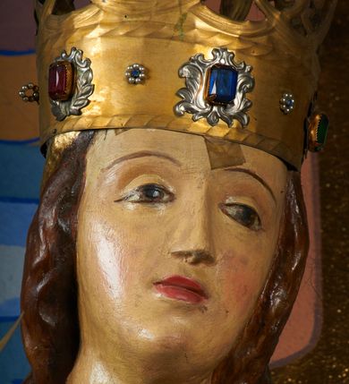 Zdjęcie nr 11: Rzeźba pełnoplastyczna, przyścienna, drążona od tyłu, ustawiona na konsoli. Maria stoi w lekkim kontrapoście, ciężar ciała opierając na lewej nodze, prawą lekko uginając w kolanie. Lewą ręką podtrzymuje siedzące na jej ramieniu Dzieciątko, w prawej ugiętej w łokciu i wysuniętej lekko do przodu trzyma błyskawicę. Twarz pociągła, z długim, prostym, wąskim nosem, oczami o migdałowym wykroju, regularnymi łukami brwiowymi oraz wąskimi ustami, okolona długimi, ciemnobrązowymi włosami, z przedziałkiem pośrodku głowy, opadającymi na ramiona dwoma skręcającymi się w pukle pasmami. Maria ubrana w długą, czerwoną suknię z wąskimi rękawami oraz złoty płaszcz spięty na piersi, przerzucony z przodu przez lewe ramię, układający się pośrodku w trzy płytkie misowe fałdy, po bokach formujący się w dwa festony. Dzieciątko siedzi wyprostowane w ramionach Matki, zwrócone przodem do widza, w prawej rączce trzymając krzyż, w lewej jabłko królewskie. Głowa pochylona lekko na lewe ramię; okrągła twarz z małym, zadartym nosem, wąskimi ustami, niewielkimi oczami i regularnymi łukami brwiowymi, okolona krótkimi ciemnobrązowymi włosami. Jezus ubrany w długą białą szatę układającą się w proste, bardzo płytkie fałdy. Na głowach nowsze korony otwarte.