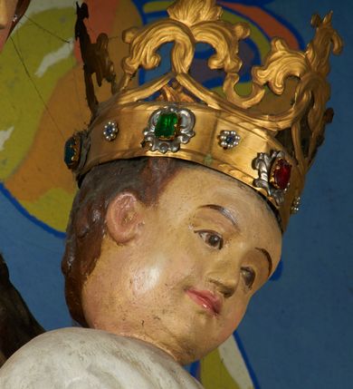 Zdjęcie nr 3: Rzeźba pełnoplastyczna, przyścienna, drążona od tyłu, ustawiona na konsoli. Maria stoi w lekkim kontrapoście, ciężar ciała opierając na lewej nodze, prawą lekko uginając w kolanie. Lewą ręką podtrzymuje siedzące na jej ramieniu Dzieciątko, w prawej ugiętej w łokciu i wysuniętej lekko do przodu trzyma błyskawicę. Twarz pociągła, z długim, prostym, wąskim nosem, oczami o migdałowym wykroju, regularnymi łukami brwiowymi oraz wąskimi ustami, okolona długimi, ciemnobrązowymi włosami, z przedziałkiem pośrodku głowy, opadającymi na ramiona dwoma skręcającymi się w pukle pasmami. Maria ubrana w długą, czerwoną suknię z wąskimi rękawami oraz złoty płaszcz spięty na piersi, przerzucony z przodu przez lewe ramię, układający się pośrodku w trzy płytkie misowe fałdy, po bokach formujący się w dwa festony. Dzieciątko siedzi wyprostowane w ramionach Matki, zwrócone przodem do widza, w prawej rączce trzymając krzyż, w lewej jabłko królewskie. Głowa pochylona lekko na lewe ramię; okrągła twarz z małym, zadartym nosem, wąskimi ustami, niewielkimi oczami i regularnymi łukami brwiowymi, okolona krótkimi ciemnobrązowymi włosami. Jezus ubrany w długą białą szatę układającą się w proste, bardzo płytkie fałdy. Na głowach nowsze korony otwarte.