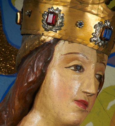 Zdjęcie nr 12: Rzeźba pełnoplastyczna, przyścienna, drążona od tyłu, ustawiona na konsoli. Maria stoi w lekkim kontrapoście, ciężar ciała opierając na lewej nodze, prawą lekko uginając w kolanie. Lewą ręką podtrzymuje siedzące na jej ramieniu Dzieciątko, w prawej ugiętej w łokciu i wysuniętej lekko do przodu trzyma błyskawicę. Twarz pociągła, z długim, prostym, wąskim nosem, oczami o migdałowym wykroju, regularnymi łukami brwiowymi oraz wąskimi ustami, okolona długimi, ciemnobrązowymi włosami, z przedziałkiem pośrodku głowy, opadającymi na ramiona dwoma skręcającymi się w pukle pasmami. Maria ubrana w długą, czerwoną suknię z wąskimi rękawami oraz złoty płaszcz spięty na piersi, przerzucony z przodu przez lewe ramię, układający się pośrodku w trzy płytkie misowe fałdy, po bokach formujący się w dwa festony. Dzieciątko siedzi wyprostowane w ramionach Matki, zwrócone przodem do widza, w prawej rączce trzymając krzyż, w lewej jabłko królewskie. Głowa pochylona lekko na lewe ramię; okrągła twarz z małym, zadartym nosem, wąskimi ustami, niewielkimi oczami i regularnymi łukami brwiowymi, okolona krótkimi ciemnobrązowymi włosami. Jezus ubrany w długą białą szatę układającą się w proste, bardzo płytkie fałdy. Na głowach nowsze korony otwarte.