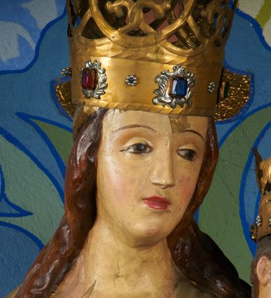 Zdjęcie nr 10: Rzeźba pełnoplastyczna, przyścienna, drążona od tyłu, ustawiona na konsoli. Maria stoi w lekkim kontrapoście, ciężar ciała opierając na lewej nodze, prawą lekko uginając w kolanie. Lewą ręką podtrzymuje siedzące na jej ramieniu Dzieciątko, w prawej ugiętej w łokciu i wysuniętej lekko do przodu trzyma błyskawicę. Twarz pociągła, z długim, prostym, wąskim nosem, oczami o migdałowym wykroju, regularnymi łukami brwiowymi oraz wąskimi ustami, okolona długimi, ciemnobrązowymi włosami, z przedziałkiem pośrodku głowy, opadającymi na ramiona dwoma skręcającymi się w pukle pasmami. Maria ubrana w długą, czerwoną suknię z wąskimi rękawami oraz złoty płaszcz spięty na piersi, przerzucony z przodu przez lewe ramię, układający się pośrodku w trzy płytkie misowe fałdy, po bokach formujący się w dwa festony. Dzieciątko siedzi wyprostowane w ramionach Matki, zwrócone przodem do widza, w prawej rączce trzymając krzyż, w lewej jabłko królewskie. Głowa pochylona lekko na lewe ramię; okrągła twarz z małym, zadartym nosem, wąskimi ustami, niewielkimi oczami i regularnymi łukami brwiowymi, okolona krótkimi ciemnobrązowymi włosami. Jezus ubrany w długą białą szatę układającą się w proste, bardzo płytkie fałdy. Na głowach nowsze korony otwarte.