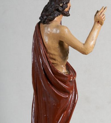 Zdjęcie nr 4: Rzeźba pełna, ustawiona jest na niskiej podstawie w formie płyty oraz na wypukłym postumencie imitującym fragment gruntu. Chrystus ukazany jest w całej postaci, frontalnie, w wykroku, z prawą ręką uniesioną w geście błogosławieństwa, w lewej trzyma drzewce zakończone krzyżem, z brakującą chorągwią. Jego twarz jest szczupła i pociągła, o dużych oczach, prostym nosie i pełnych ustach, okolona krótką, brązową brodą skręconą w dwa pukle oraz brązowymi, silnie kręconymi włosami opadającymi na plecy. Biodra Chrystusa przepasane są krótkim perizonium, zaś na jego lewym ramieniu zawieszony jest czerwony płaszcz, który otacza diagonalnie postać i zarzucony jest z przodu postaci na lewym przedramieniu, odsłaniając tors i nogi. Ciało bardzo wychudzone, o podkreślonych liniach żeber i mostka klatki piersiowej, z zaznaczonymi śladami męki. Polichromia ciała jest naturalistyczna, perizonium pozłacane, a drzewce pomalowane na kolor brązowy.



