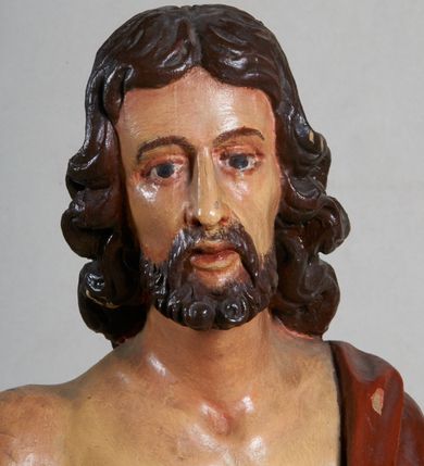 Zdjęcie nr 8: Rzeźba pełna, ustawiona jest na niskiej podstawie w formie płyty oraz na wypukłym postumencie imitującym fragment gruntu. Chrystus ukazany jest w całej postaci, frontalnie, w wykroku, z prawą ręką uniesioną w geście błogosławieństwa, w lewej trzyma drzewce zakończone krzyżem, z brakującą chorągwią. Jego twarz jest szczupła i pociągła, o dużych oczach, prostym nosie i pełnych ustach, okolona krótką, brązową brodą skręconą w dwa pukle oraz brązowymi, silnie kręconymi włosami opadającymi na plecy. Biodra Chrystusa przepasane są krótkim perizonium, zaś na jego lewym ramieniu zawieszony jest czerwony płaszcz, który otacza diagonalnie postać i zarzucony jest z przodu postaci na lewym przedramieniu, odsłaniając tors i nogi. Ciało bardzo wychudzone, o podkreślonych liniach żeber i mostka klatki piersiowej, z zaznaczonymi śladami męki. Polichromia ciała jest naturalistyczna, perizonium pozłacane, a drzewce pomalowane na kolor brązowy.



