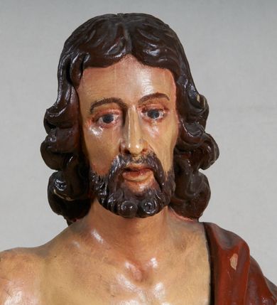 Zdjęcie nr 9: Rzeźba pełna, ustawiona jest na niskiej podstawie w formie płyty oraz na wypukłym postumencie imitującym fragment gruntu. Chrystus ukazany jest w całej postaci, frontalnie, w wykroku, z prawą ręką uniesioną w geście błogosławieństwa, w lewej trzyma drzewce zakończone krzyżem, z brakującą chorągwią. Jego twarz jest szczupła i pociągła, o dużych oczach, prostym nosie i pełnych ustach, okolona krótką, brązową brodą skręconą w dwa pukle oraz brązowymi, silnie kręconymi włosami opadającymi na plecy. Biodra Chrystusa przepasane są krótkim perizonium, zaś na jego lewym ramieniu zawieszony jest czerwony płaszcz, który otacza diagonalnie postać i zarzucony jest z przodu postaci na lewym przedramieniu, odsłaniając tors i nogi. Ciało bardzo wychudzone, o podkreślonych liniach żeber i mostka klatki piersiowej, z zaznaczonymi śladami męki. Polichromia ciała jest naturalistyczna, perizonium pozłacane, a drzewce pomalowane na kolor brązowy.



