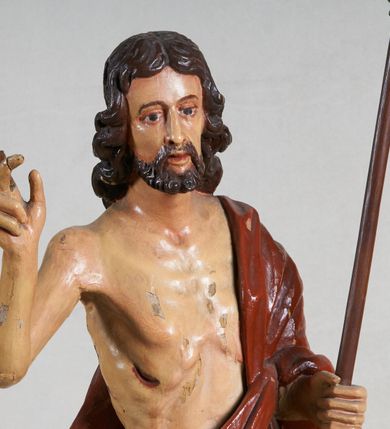 Zdjęcie nr 7: Rzeźba pełna, ustawiona jest na niskiej podstawie w formie płyty oraz na wypukłym postumencie imitującym fragment gruntu. Chrystus ukazany jest w całej postaci, frontalnie, w wykroku, z prawą ręką uniesioną w geście błogosławieństwa, w lewej trzyma drzewce zakończone krzyżem, z brakującą chorągwią. Jego twarz jest szczupła i pociągła, o dużych oczach, prostym nosie i pełnych ustach, okolona krótką, brązową brodą skręconą w dwa pukle oraz brązowymi, silnie kręconymi włosami opadającymi na plecy. Biodra Chrystusa przepasane są krótkim perizonium, zaś na jego lewym ramieniu zawieszony jest czerwony płaszcz, który otacza diagonalnie postać i zarzucony jest z przodu postaci na lewym przedramieniu, odsłaniając tors i nogi. Ciało bardzo wychudzone, o podkreślonych liniach żeber i mostka klatki piersiowej, z zaznaczonymi śladami męki. Polichromia ciała jest naturalistyczna, perizonium pozłacane, a drzewce pomalowane na kolor brązowy.



