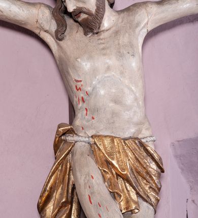 Zdjęcie nr 2: Figura umarłego Chrystusa została przybita do prostego krzyża trzema gwoździami. Jego ciało ukazane jest w lekkim zwisie, o niemal horyzontalnie rozłożonych ramionach, z głową opadającą na prawy bark, z lekko ugiętymi kolanami i stopami skrzyżowanymi w układzie prawa na lewą. Twarz Chrystusa jest szczupła, zwężająca się mocno ku dołowi, z okrągłymi, zamkniętymi oczami, z niewielkim, wąskim nosem i z małymi, rozchylonymi ustami, okolona krótką brązową, brodą, układającą się w dwa pukle oraz brązowymi, kręconym włosami opadającymi na prawe ramię. Ciało Chrystusa jest szczupłe, o delikatnym modelunku, z zaznaczoną muskulaturą ramion i nóg, z wyraźnie zarysowanymi żebrami i mostkiem klatki piersiowej. Perizonium zawieszone na sznurze, częściowo odsłaniające biodra i prawe udo, ze zwisem tkaniny opadającym wzdłuż prawego boku Chrystusa. Na głowie korona cierniowa. Na górnym zakończeniu pionowej belki krzyża kartusz z napisem „I.N.R.I.”. Polichromia karnacji ciała naturalistyczna, z zaznaczonymi śladami męki, tkanina perizonium i korona cierniowa pozłacane. 
