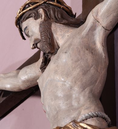 Zdjęcie nr 4: Figura umarłego Chrystusa została przybita do prostego krzyża trzema gwoździami. Jego ciało ukazane jest w lekkim zwisie, o niemal horyzontalnie rozłożonych ramionach, z głową opadającą na prawy bark, z lekko ugiętymi kolanami i stopami skrzyżowanymi w układzie prawa na lewą. Twarz Chrystusa jest szczupła, zwężająca się mocno ku dołowi, z okrągłymi, zamkniętymi oczami, z niewielkim, wąskim nosem i z małymi, rozchylonymi ustami, okolona krótką brązową, brodą, układającą się w dwa pukle oraz brązowymi, kręconym włosami opadającymi na prawe ramię. Ciało Chrystusa jest szczupłe, o delikatnym modelunku, z zaznaczoną muskulaturą ramion i nóg, z wyraźnie zarysowanymi żebrami i mostkiem klatki piersiowej. Perizonium zawieszone na sznurze, częściowo odsłaniające biodra i prawe udo, ze zwisem tkaniny opadającym wzdłuż prawego boku Chrystusa. Na głowie korona cierniowa. Na górnym zakończeniu pionowej belki krzyża kartusz z napisem „I.N.R.I.”. Polichromia karnacji ciała naturalistyczna, z zaznaczonymi śladami męki, tkanina perizonium i korona cierniowa pozłacane. 
