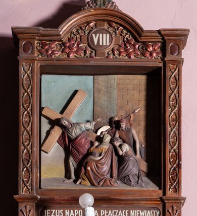Zdjęcie nr 12: Stacje Drogi krzyżowej w kształcie stojących prostokątów zostały ujęte architektoniczną ramą. Obrazy ustawiono na cokole, po bokach są flankowane dwoma pilastrami, podtrzymującymi wyłamane belkowanie, zamknięte gzymsem w kształcie łuku nadwieszonego. Na szczycie, w rzeźbionych owocach winogron osadzono grecki krzyżyk o trójlistnie zakończonych ramionach z uskokami. Pilastry są zdobione symetryczną wicią cierniową, a pole zwieńczenia bogato dekorowane wicią roślinną złożoną z bujnych, czerwonych kwiatów otaczających numer stacji umieszczony w owalu na tle krzyżyka greckiego. 
Sceny przeważnie wielopostaciowe, płaskorzeźbione, barwnie polichromowane. Postacie o poprawnej anatomii ciała, poruszone, na pierwszym planie bardziej wypukłe. Tło błękitne, malowane. W partii cokołu umieszczono malowane tytuły stacji:
I. „JEZUS NA ŚMIERĆ OSĄDZONY.”
II. „JEZUS BIERZE KRZYŻ NA RAMIONA.”
III. „JEZUS PIERWSZY RAZ UPADA.”
IV. „JEZUS SPOTYKA NAJŚW(IĘTSZĄ) MATKĘ SWOJĄ”
V. „SZYMON CYR(ENEJCZYK) POMAGA NIEŚĆ KRZYŻ JEZUSA”
VI. „ŚW(IĘTA) WERONIKA OCIERA TWARZ JEZUSA”
VII. „JEZUS DRUGI RAZ UPADA”
VIII. „JEZUS NAPOTYKA PŁACZĄCE NIEWIASTY”
IX. „JEZUS TRZECI RAZ UPADA.”
X. „JEZUS Z SZAT OBNAŻONY”
XI. „JEZUS DO KRZYŻA PRZYBITY”
XII. „JEZUS NA KRZYŻU UMIERA.”
XIII. „JEZUS Z KRZYŻA ZDJĘTY.”
XIV. „JEZUS DO GROBU ZŁOŻONY.”
