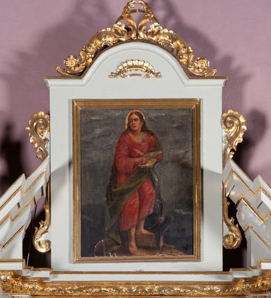 Zdjęcie nr 2: Obraz w formie stojącego prostokąta. W centrum kompozycji ukazany św. Jan Ewangelista w postawie stojącej, frontalnie, z lewą stopą wspartą na niskim cokole, piszący piórem w otwartej księdze podtrzymywanej lewą ręką. Twarz szeroka, o młodzieńczych rysach, z długim i szerokim nosem, wzrokiem skierowanym ku górze. Włosy długie, z przedziałkiem pośrodku, opadające na plecy i ramiona. Wokół głowy, złoty i kolisty nimb. Święty ubrany jest w długą, czerwoną suknię z długimi rękawami, z szerokim dekoltem, odsłaniającą bose stopy oraz zielony płaszcz zarzucony na plecy. U stóp świętego, po prawej stronie obrazu orzeł z kałamarzem w dziobie. Tło szare.
