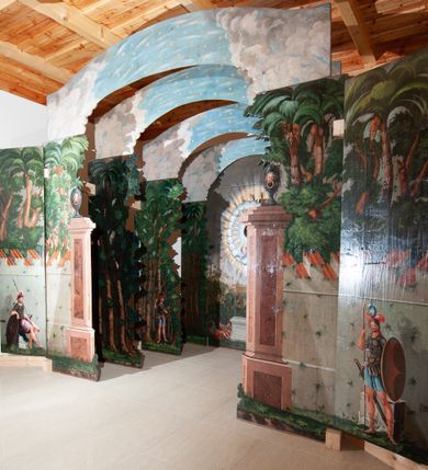 Zdjęcie nr 13: Oprawa grobu Pańskiego kulisowa, pięciopłaszczyznowa. Pierwszy plan tworzy iluzjonistyczna dekoracja, utworzona z bramy składającej się z dwóch filarów zwieńczonych wazonami z antabami oraz muru z krenelażem. Na tle muru ukazani dwaj rzymscy legioniści, po lewej stronie siedzący, po prawej stojący. W tle bogata roślinność egzotyczna z palmami. Na pozostałych planach namalowana roślinność leśna z egzotycznymi gatunkami palm. Na trzeciej parze kulis  przedstawieni dwaj rzymscy legioniści, lewy w pozycji stojącej, prawy leżącej, z głową wspartą na ręce. Wszystkie cztery płaszczyzny zamknięte łukami z namalowanym błękitnym niebem z gwiazdami, ujętym obłokami. 
Na ścianie zamykającej dekorację ukazano kamienny grób, po bokach którego siedzi i leży po trzech legionistów rzymskich z każdej strony. Nad nimi namalowane zalesione wzgórze Golgoty z trzema krzyżami, przed którymi stoi płaczący anioł. W tle widoczny jest pejzaż Jerozolimy, nad którym ukazano zaćmione słońce. W górnej części ściany ukazano niebo z nałożonym medalionem utworzonym z obłoków, z dwiema uskrzydlonymi główkami anielskimi, w glorii promienistej. 



