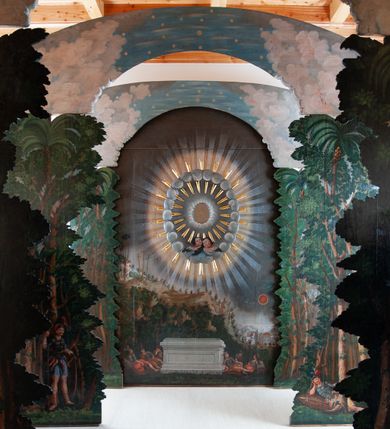 Zdjęcie nr 6: Oprawa grobu Pańskiego kulisowa, pięciopłaszczyznowa. Pierwszy plan tworzy iluzjonistyczna dekoracja, utworzona z bramy składającej się z dwóch filarów zwieńczonych wazonami z antabami oraz muru z krenelażem. Na tle muru ukazani dwaj rzymscy legioniści, po lewej stronie siedzący, po prawej stojący. W tle bogata roślinność egzotyczna z palmami. Na pozostałych planach namalowana roślinność leśna z egzotycznymi gatunkami palm. Na trzeciej parze kulis  przedstawieni dwaj rzymscy legioniści, lewy w pozycji stojącej, prawy leżącej, z głową wspartą na ręce. Wszystkie cztery płaszczyzny zamknięte łukami z namalowanym błękitnym niebem z gwiazdami, ujętym obłokami. 
Na ścianie zamykającej dekorację ukazano kamienny grób, po bokach którego siedzi i leży po trzech legionistów rzymskich z każdej strony. Nad nimi namalowane zalesione wzgórze Golgoty z trzema krzyżami, przed którymi stoi płaczący anioł. W tle widoczny jest pejzaż Jerozolimy, nad którym ukazano zaćmione słońce. W górnej części ściany ukazano niebo z nałożonym medalionem utworzonym z obłoków, z dwiema uskrzydlonymi główkami anielskimi, w glorii promienistej. 



