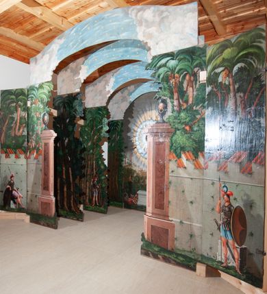 Zdjęcie nr 2: Oprawa grobu Pańskiego kulisowa, pięciopłaszczyznowa. Pierwszy plan tworzy iluzjonistyczna dekoracja, utworzona z bramy składającej się z dwóch filarów zwieńczonych wazonami z antabami oraz muru z krenelażem. Na tle muru ukazani dwaj rzymscy legioniści, po lewej stronie siedzący, po prawej stojący. W tle bogata roślinność egzotyczna z palmami. Na pozostałych planach namalowana roślinność leśna z egzotycznymi gatunkami palm. Na trzeciej parze kulis  przedstawieni dwaj rzymscy legioniści, lewy w pozycji stojącej, prawy leżącej, z głową wspartą na ręce. Wszystkie cztery płaszczyzny zamknięte łukami z namalowanym błękitnym niebem z gwiazdami, ujętym obłokami. 
Na ścianie zamykającej dekorację ukazano kamienny grób, po bokach którego siedzi i leży po trzech legionistów rzymskich z każdej strony. Nad nimi namalowane zalesione wzgórze Golgoty z trzema krzyżami, przed którymi stoi płaczący anioł. W tle widoczny jest pejzaż Jerozolimy, nad którym ukazano zaćmione słońce. W górnej części ściany ukazano niebo z nałożonym medalionem utworzonym z obłoków, z dwiema uskrzydlonymi główkami anielskimi, w glorii promienistej. 



