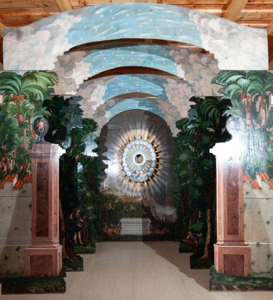 Zdjęcie nr 1: Oprawa grobu Pańskiego kulisowa, pięciopłaszczyznowa. Pierwszy plan tworzy iluzjonistyczna dekoracja, utworzona z bramy składającej się z dwóch filarów zwieńczonych wazonami z antabami oraz muru z krenelażem. Na tle muru ukazani dwaj rzymscy legioniści, po lewej stronie siedzący, po prawej stojący. W tle bogata roślinność egzotyczna z palmami. Na pozostałych planach namalowana roślinność leśna z egzotycznymi gatunkami palm. Na trzeciej parze kulis  przedstawieni dwaj rzymscy legioniści, lewy w pozycji stojącej, prawy leżącej, z głową wspartą na ręce. Wszystkie cztery płaszczyzny zamknięte łukami z namalowanym błękitnym niebem z gwiazdami, ujętym obłokami. 
Na ścianie zamykającej dekorację ukazano kamienny grób, po bokach którego siedzi i leży po trzech legionistów rzymskich z każdej strony. Nad nimi namalowane zalesione wzgórze Golgoty z trzema krzyżami, przed którymi stoi płaczący anioł. W tle widoczny jest pejzaż Jerozolimy, nad którym ukazano zaćmione słońce. W górnej części ściany ukazano niebo z nałożonym medalionem utworzonym z obłoków, z dwiema uskrzydlonymi główkami anielskimi, w glorii promienistej. 



