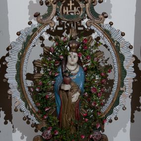 Zdjęcie nr 1: Na postumencie o kształcie wolutowym zaopatrzonym w otwory na drążki do noszenia, przyozdobionym żłobkowaniem, wolutami w narożach oraz po jednej róży na bokach umieszczona została dwustronnie rzeźbiona, żłobkowana, owalna rama, przyozdobiona kulkami zawieszonymi na metalowych uchwytach, zwieńczona dwiema wolutami z różyczką na jednym końcu podtrzymującymi monogram IHS w wieńcu laurowym z dwiema wiszącymi kulkami, powyżej dwiema półwolutami przyozdobionymi wiszącymi kulkami i przytrzymującymi czerwoną koronę w typie zamkniętym z krzyżykiem równoramiennym, w zwieńczeniu dwa wolutowe kabłąki, na nich rozeta. 
Dekoracja malarska feretronu w kolorze zielonym, brązowym, białym i złotym.
Figura Matki Bożej w glorii promienistej. Matka Boża ukazana en face, w pozycji stojącej, w prawym ręku trzyma gorejące serce. Rozpuszczone włosy opadają na plecy i prawy bok, twarz owalna, wąskie brwi, niebieskie, małe oczy i małe, wąskie usta. Ubrana w złotą suknię przepasaną złotym paskiem, niebieski płaszcz z czerwonym podszyciem i złotą lamówką spięty na dekolcie. Na szyi zawieszony sznur korali. Na głowie korona w typie zamkniętym zwieńczona krzyżykiem umieszonym na złotej kulce.